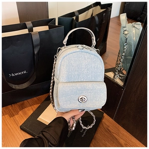 Detail of light blue denim mini backpack with silver chain straps and turn-lock buckle