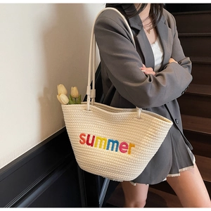Close-up of woven straw beach tote bag with colorful summer embroidery and white handles