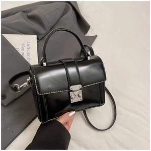 Detail of minimalist black leather crossbody bag featuring a silver square metal lock