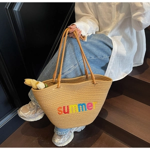 Detail of woven straw tote bag with summer embroidery and brown leather straps