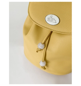 Close-up of yellow pebbled leather backpack with rabbit emblem and drawstring bead