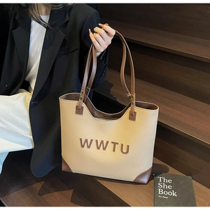 Detail view of large tote bag with embossed letters and brown leather accents