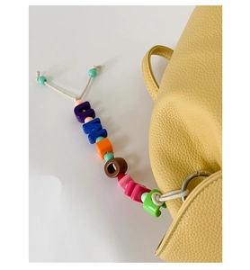 Detail of colorful letter bead charm with resin beads hanging on yellow leather bag
