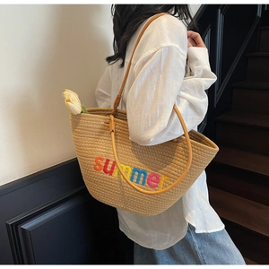 Detail of woven straw tote bag with colorful summer embroidery and leather shoulder strap