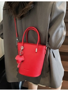 Fashionable red bucket bag in litchi grain leather with an elephant charm on a model