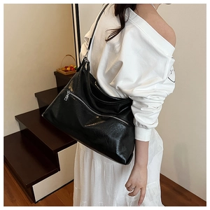 Detail of a large black glossy leather tote bag with a decorative metal diagonal zipper