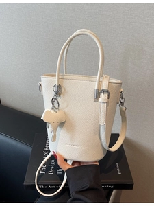 Minimalist off-white bucket bag with elephant charm on artistic book display