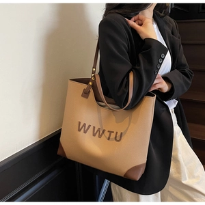 Detail view of khaki leather tote with embossed letters and dark brown straps on a model