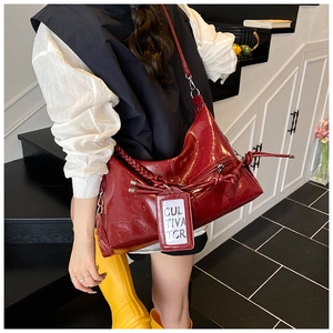 Detail of dark red glossy shoulder bag featuring woven rope trim and hanging card slot