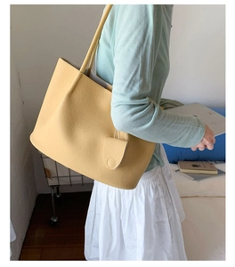Detail einer ingwergelben Leder-Tote-Bag mit Litschi-Muster am Model im Wohnzimmer