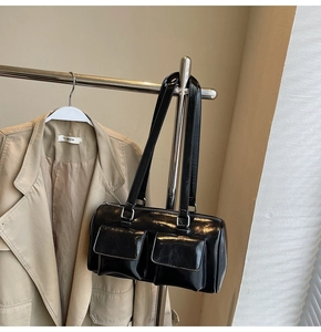 Detailed close-up of glossy black underarm bag with double front pockets on display
