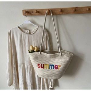 Detail view of woven tote bag with colorful summer embroidery on a wooden hook