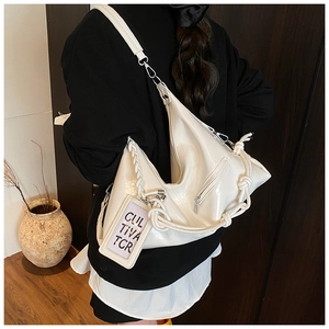Detail of a white patent leather hobo bag with braided charms and silver metal hardware