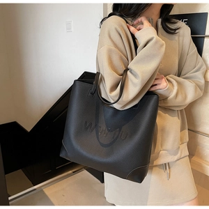 Detail shot of black pebbled leather tote bag with embossed logo and slim shoulder straps
