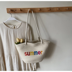 Detail of cream woven tote bag with colorful Summer embroidery on a wooden hook