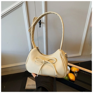 Detail of a creamy white half-moon shoulder bag featuring stylish bow accents and lychee texture