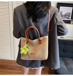 Détail du sac fourre-tout tressé beige avec anses en cuir marron et breloque fleurie