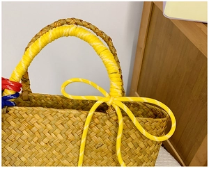 Detail of hand-woven straw tote with vibrant multi-colored rope handles and yellow bow accent