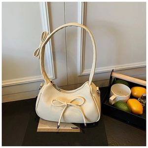 Detail of a creamy white crescent bag with bow accents and premium litchi leather texture
