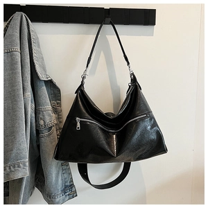 Detail of a black leather tote bag with a metal zipper and adjustable strap hanging on a wall