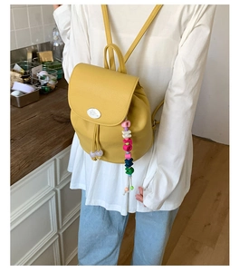 Detail of a bright yellow mini backpack with litchi texture and colorful bead pendant