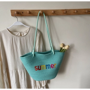 Detail of mint green woven tote bag with summer embroidery hanging on a wall