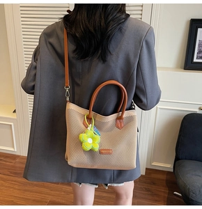 Détail d'un sac cabas tissé avec des anses en cuir marron et un charm fleur en peluche