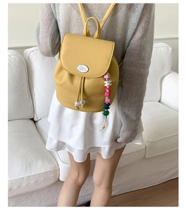 Detail of yellow lychee leather backpack featuring drawstring and beaded charm accessory