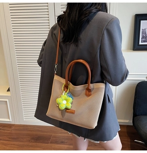 Détail du sac cabas en maille beige avec anses en cuir marron et breloque fleur verte