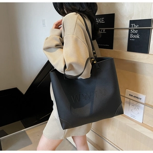 Detail of a black large-capacity tote bag with embossed letters worn by a model