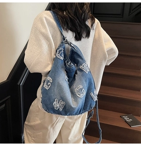 Detail of blue denim tote bag with distressed white letter patches on a grey sweatshirt