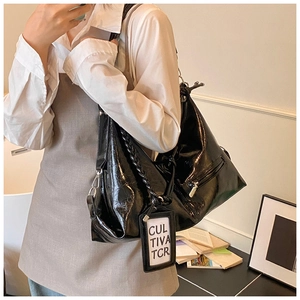 Close-up of black glossy leather tote bag featuring woven handle and side zip pocket