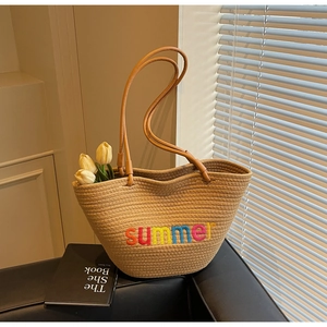 Close-up of beige woven tote bag with colorful summer embroidery and long brown straps