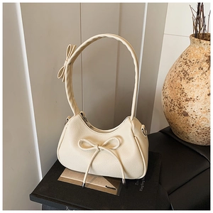 Chic beige bow crescent shoulder bag with lychee grain leather on a book prop