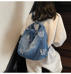 Detail of vintage denim tote bag with frayed letter patchwork and metallic adjustment ring