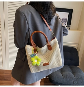 Détail du sac cabas tissé avec anses en cuir marron et pendentif fleur verte