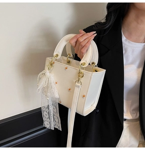 Detailed close-up of cream PU leather bag with daisy embroidery and pearl lace charm