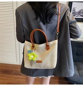 Détail du sac cabas tissé crème avec poignées en cuir marron et breloque fleurie