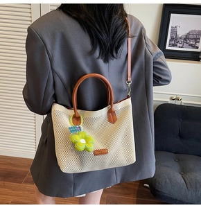 Détail du sac cabas tissé avec poignées en cuir marron et pendentif fleur verte