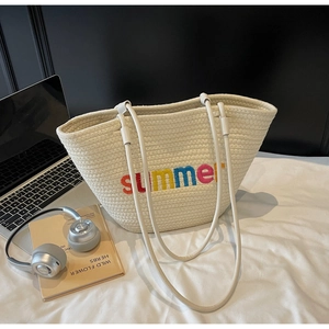 Detail of cream woven tote bag featuring colorful summer embroidery and laptop lifestyle props