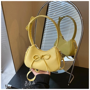 Detail of yellow lychee grain shoulder bag featuring a decorative bow and curved strap