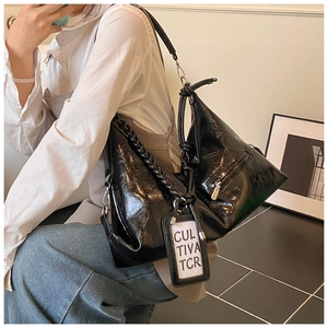Detail of glossy black patent leather tote with braided handle and silver zipper pocket