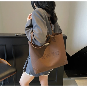 Detail of embossed WWTU lettering on a large brown leather tote bag for daily commute
