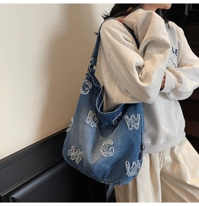 Detail of vintage denim tote bag with white distressed letter patches shown on model