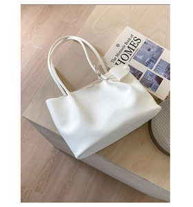 Detail einer weißen Shopper-Tasche aus genarbtem Leder mit langen Griffen auf Holz
