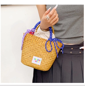 Detail of hand-woven straw basket bag featuring colorful rope bows and drawstring liner