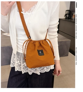 Caramel drawstring crossbody bag worn by model in a modern minimalist home setting