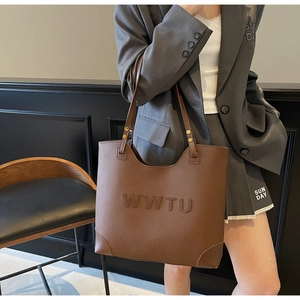 Close-up of brown large tote bag with embossed letters and pebbled leather texture