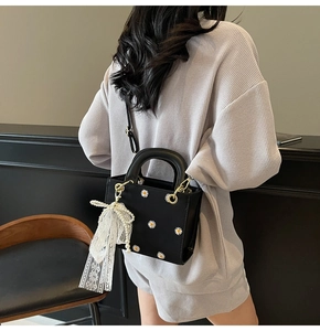 Detailed close-up of daisy embroidery on a black square crossbody bag with lace bow