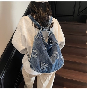 Detailed view of frayed letter patchwork and silver hardware on a denim tote bag